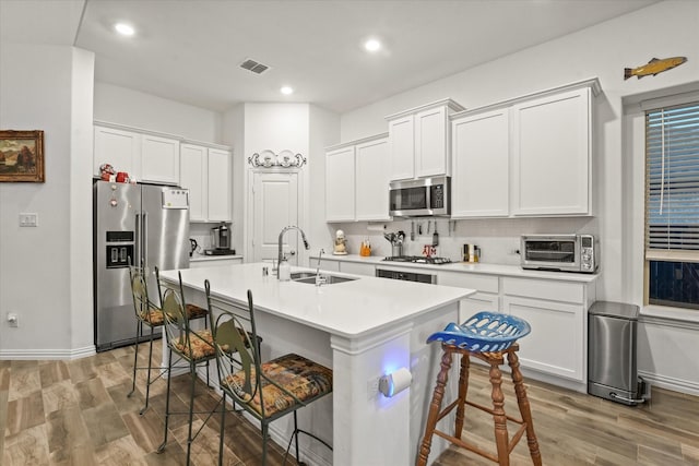 kitchen with white cabinetry, a kitchen bar, appliances with stainless steel finishes, a kitchen island with sink, and sink