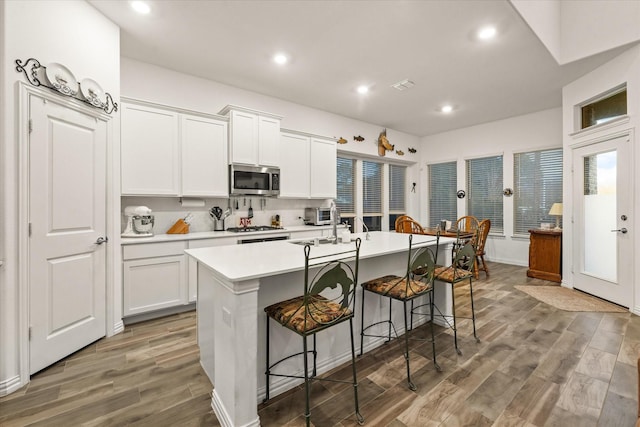 kitchen featuring white cabinets, a kitchen island with sink, a kitchen breakfast bar, and hardwood / wood-style flooring