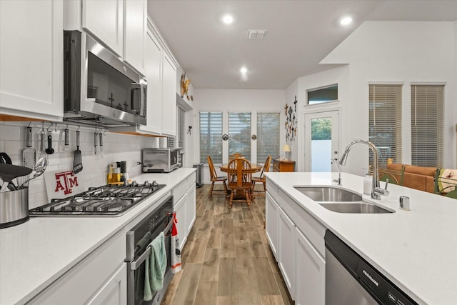 kitchen with white cabinets, stainless steel appliances, light hardwood / wood-style floors, sink, and decorative backsplash