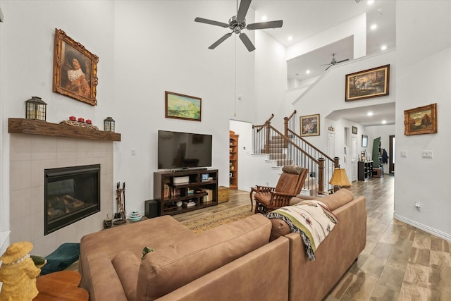 living room with ceiling fan, a tiled fireplace, and a high ceiling