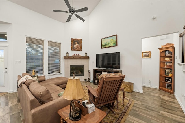 living room with ceiling fan, wood-type flooring, a tiled fireplace, and high vaulted ceiling