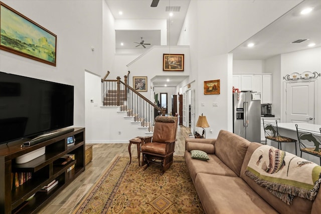 living room with light hardwood / wood-style floors, a towering ceiling, and ceiling fan