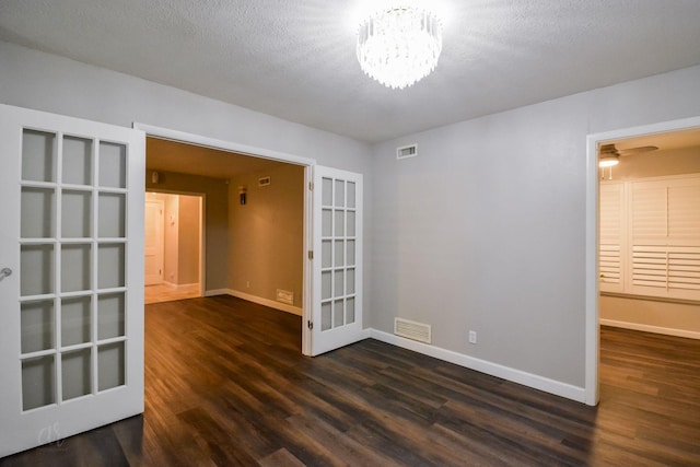 spare room featuring french doors, dark hardwood / wood-style floors, ceiling fan with notable chandelier, and a textured ceiling