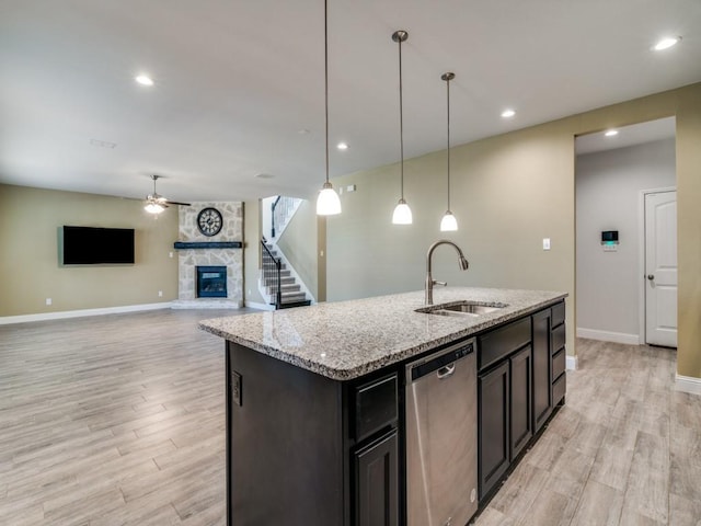 kitchen featuring dishwasher, a stone fireplace, sink, light wood-type flooring, and a center island with sink