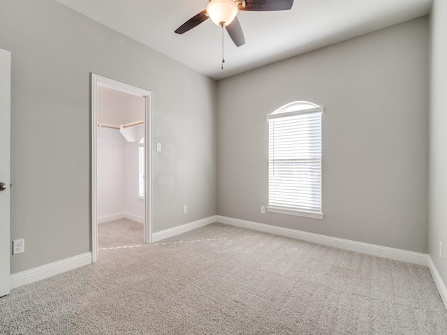 unfurnished bedroom with ceiling fan, a walk in closet, a closet, and light colored carpet