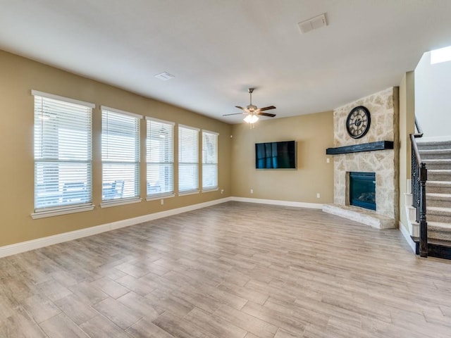 unfurnished living room featuring ceiling fan and a stone fireplace