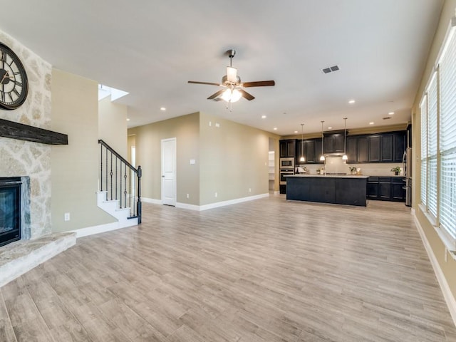 unfurnished living room featuring ceiling fan, light wood-type flooring, and a stone fireplace