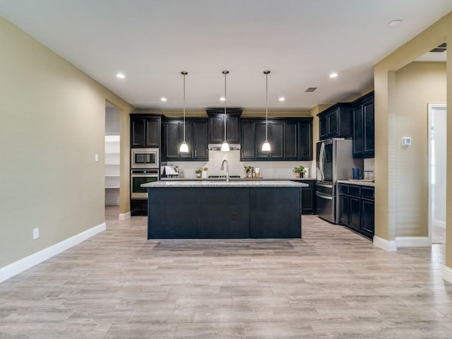 kitchen with light hardwood / wood-style floors, a center island with sink, appliances with stainless steel finishes, hanging light fixtures, and light stone countertops