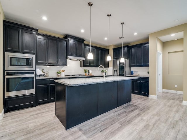 kitchen featuring decorative light fixtures, light hardwood / wood-style floors, stainless steel appliances, and an island with sink