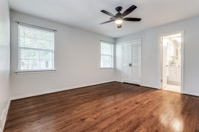 unfurnished bedroom featuring ceiling fan, ensuite bath, a closet, dark hardwood / wood-style flooring, and multiple windows