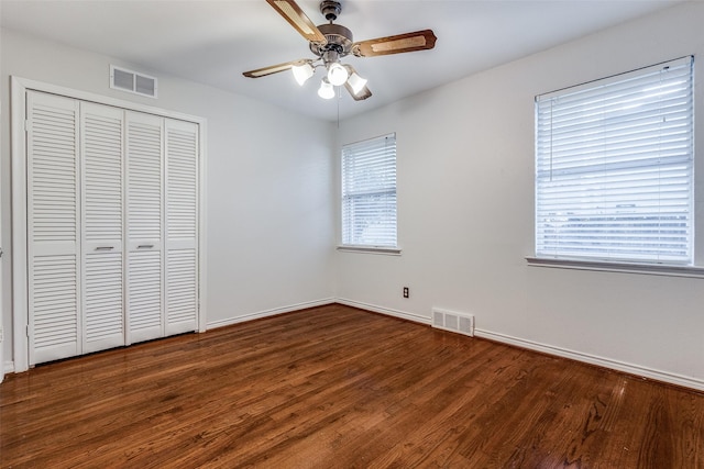 unfurnished bedroom featuring ceiling fan, dark hardwood / wood-style flooring, a closet, and multiple windows