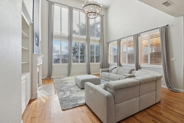 living room featuring a notable chandelier, light hardwood / wood-style flooring, a healthy amount of sunlight, and a high ceiling