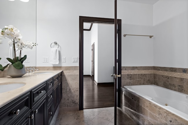 bathroom with tile patterned flooring, tiled tub, and vanity