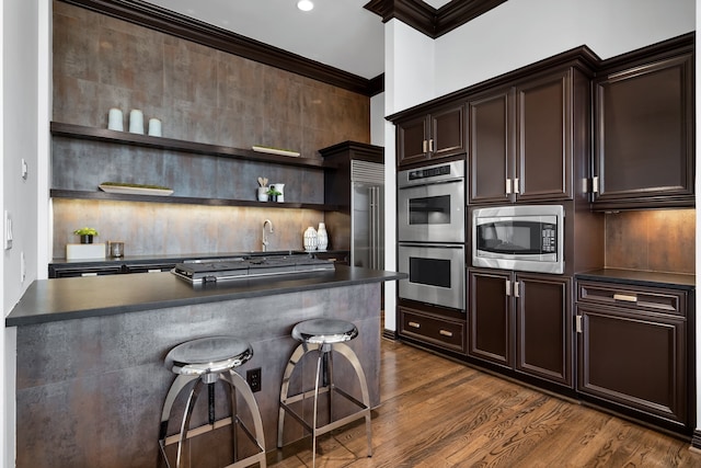 kitchen featuring a breakfast bar, dark brown cabinets, crown molding, stainless steel appliances, and dark hardwood / wood-style flooring