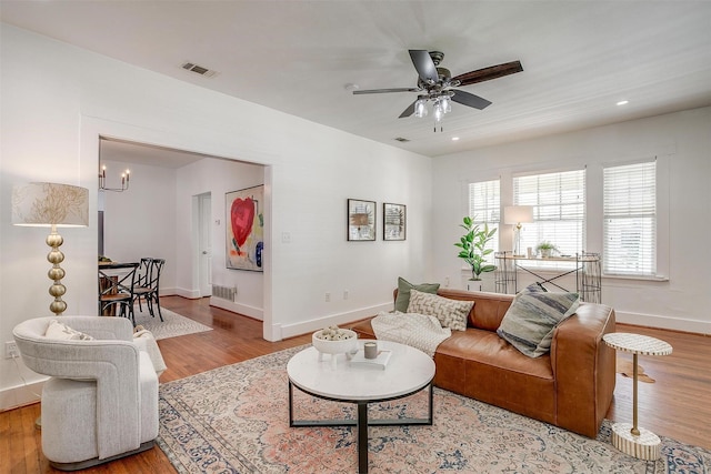 living room with ceiling fan with notable chandelier and light hardwood / wood-style floors