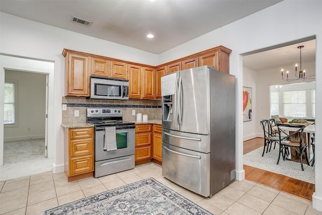 kitchen with decorative backsplash, stainless steel appliances, light tile patterned floors, light stone counters, and a chandelier