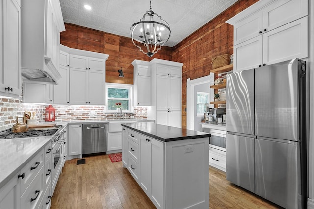 kitchen with white cabinets, appliances with stainless steel finishes, decorative light fixtures, wooden walls, and an inviting chandelier