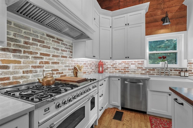 kitchen with stainless steel appliances, custom exhaust hood, white cabinetry, and sink