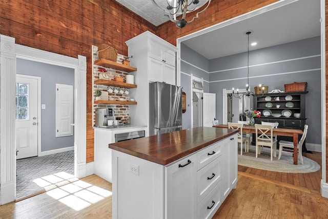 kitchen featuring white cabinets, stainless steel fridge, wooden counters, and a notable chandelier