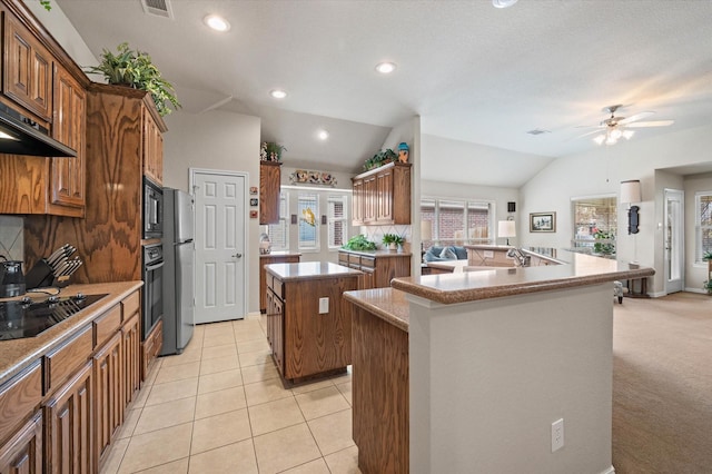 kitchen with lofted ceiling, ceiling fan, a center island with sink, black appliances, and light carpet