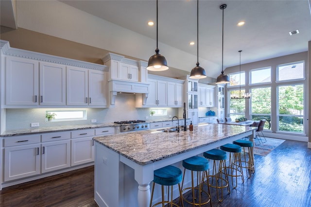 kitchen with a center island with sink, hanging light fixtures, a kitchen breakfast bar, white cabinets, and light stone counters