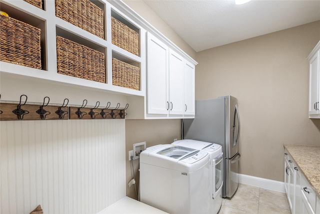 clothes washing area featuring light tile patterned floors, washing machine and dryer, and cabinets