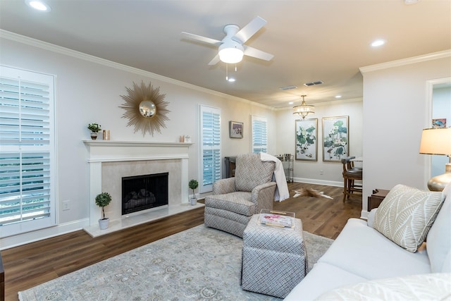 living room with dark wood-type flooring, ornamental molding, a fireplace, and ceiling fan with notable chandelier