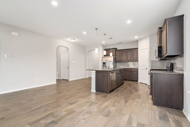 kitchen featuring appliances with stainless steel finishes, decorative light fixtures, tasteful backsplash, a kitchen island with sink, and dark brown cabinets