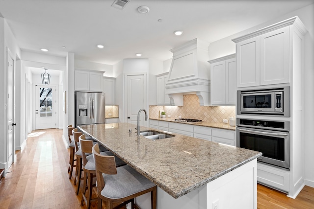 kitchen with an island with sink, sink, stainless steel appliances, and custom exhaust hood