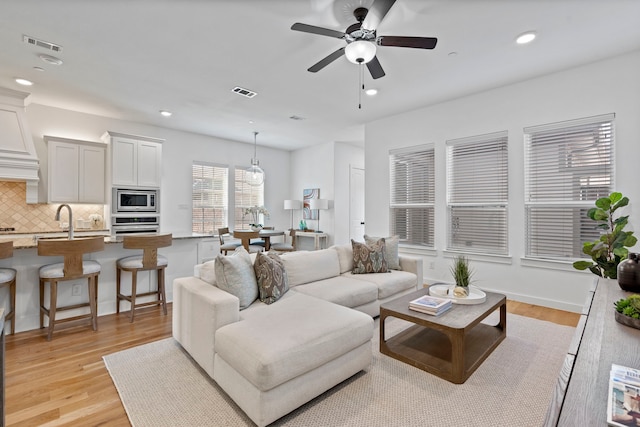 living room with ceiling fan, light wood-type flooring, and sink