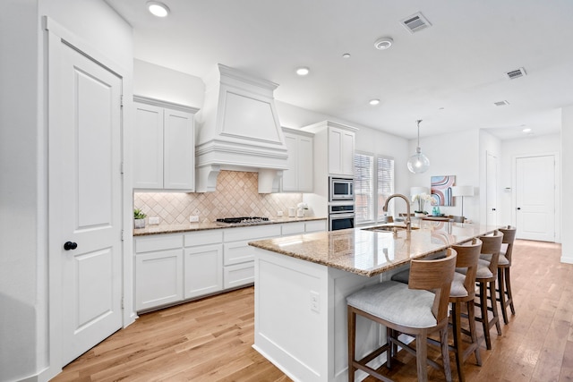 kitchen with a center island with sink, appliances with stainless steel finishes, hanging light fixtures, white cabinets, and sink