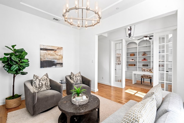 living room with ceiling fan with notable chandelier, wood-type flooring, and built in shelves