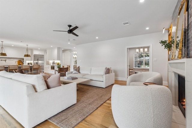 living room with ceiling fan with notable chandelier and light hardwood / wood-style flooring