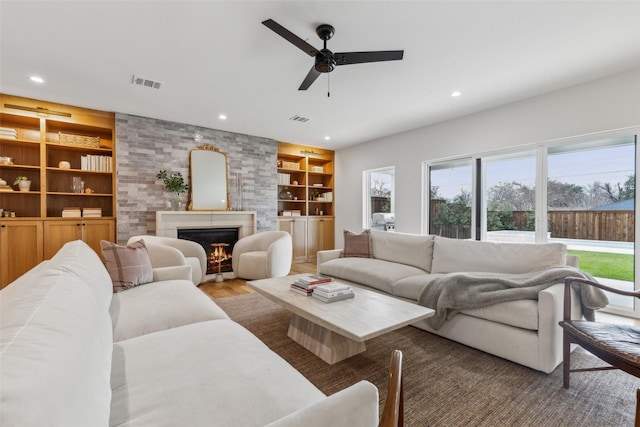 living room featuring a fireplace, built in features, wood-type flooring, and ceiling fan