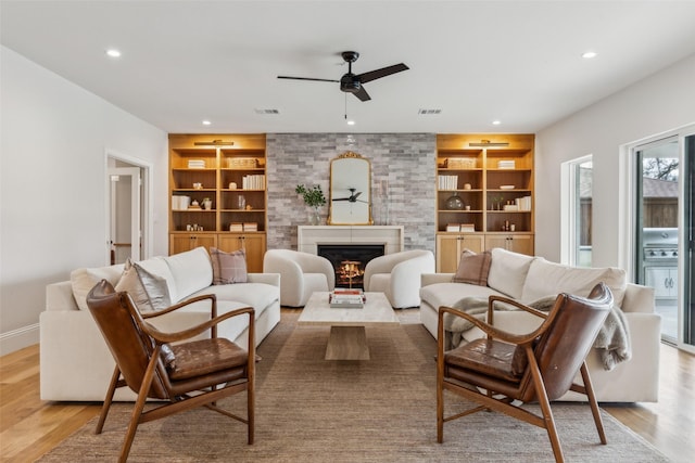 living room with ceiling fan, a large fireplace, light hardwood / wood-style floors, and built in features