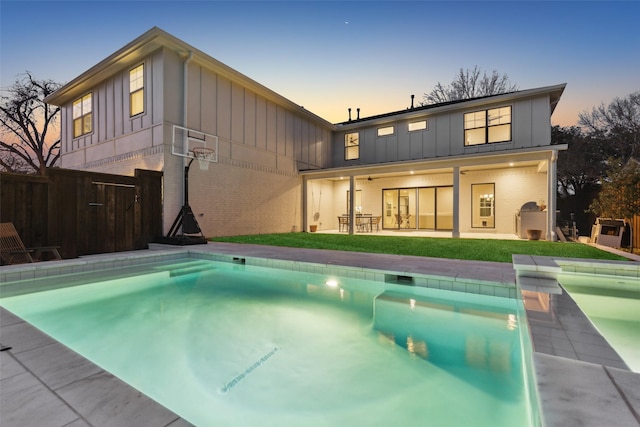 back house at dusk with ceiling fan, a yard, and a patio