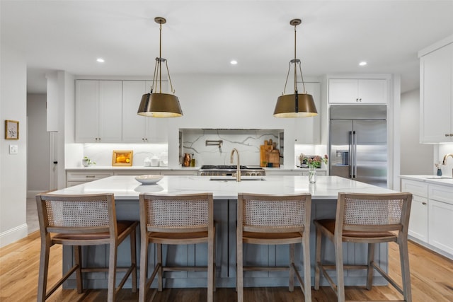 kitchen featuring decorative backsplash, a breakfast bar, stainless steel built in refrigerator, and a kitchen island with sink