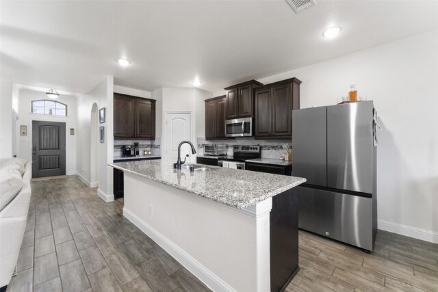 kitchen with tasteful backsplash, a center island with sink, sink, stainless steel appliances, and dark brown cabinets