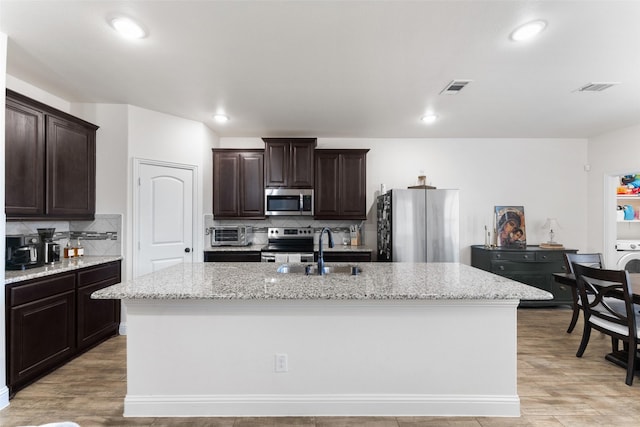 kitchen featuring sink, backsplash, stainless steel appliances, and a kitchen island with sink