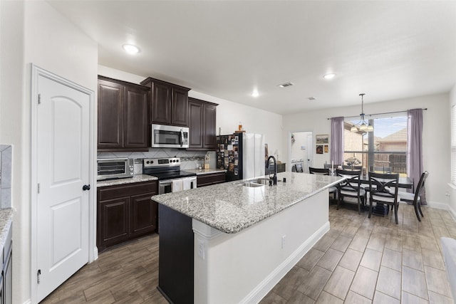 kitchen with an island with sink, appliances with stainless steel finishes, a chandelier, pendant lighting, and sink