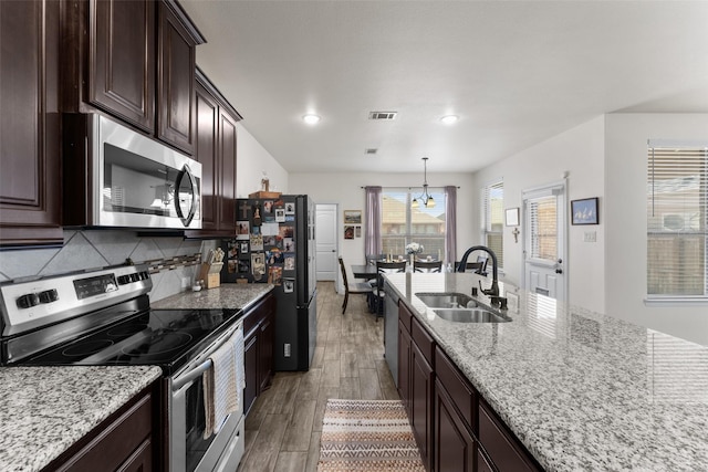 kitchen featuring appliances with stainless steel finishes, decorative light fixtures, sink, a notable chandelier, and light stone counters