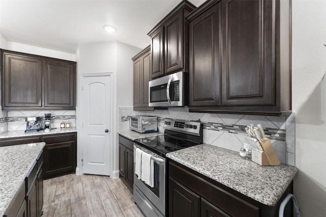 kitchen with light hardwood / wood-style floors, light stone counters, decorative backsplash, and stainless steel appliances