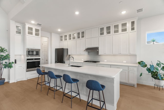 kitchen featuring a center island with sink, sink, a breakfast bar area, stainless steel appliances, and white cabinets