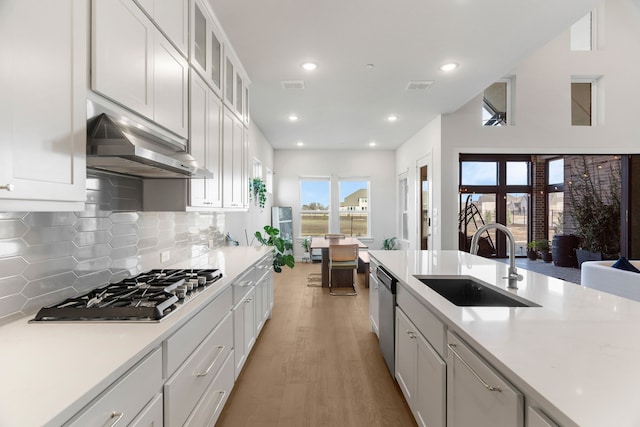 kitchen with tasteful backsplash, sink, white cabinetry, light wood-type flooring, and appliances with stainless steel finishes