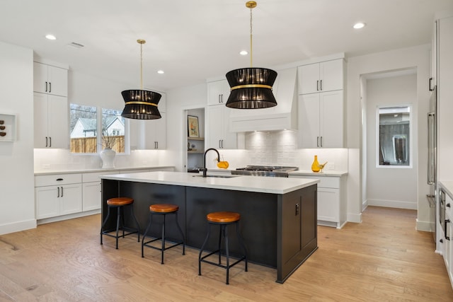 kitchen featuring pendant lighting, light hardwood / wood-style floors, a kitchen island with sink, and white cabinets