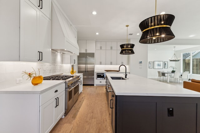 kitchen featuring sink, high end appliances, custom range hood, pendant lighting, and white cabinets