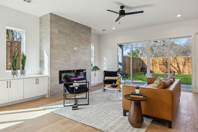 living room with ceiling fan, plenty of natural light, a fireplace, and light wood-type flooring