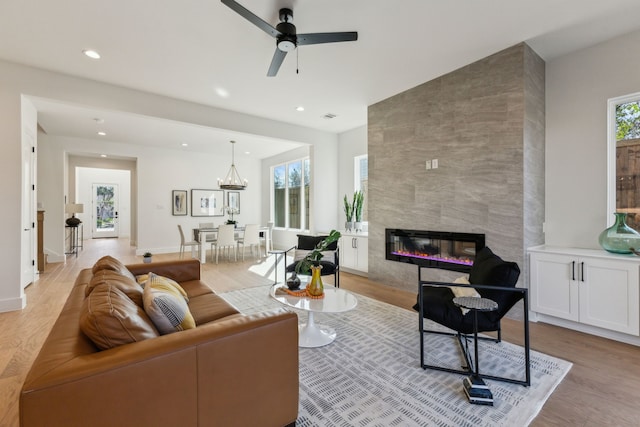 living room with a tiled fireplace, plenty of natural light, ceiling fan with notable chandelier, and light hardwood / wood-style flooring