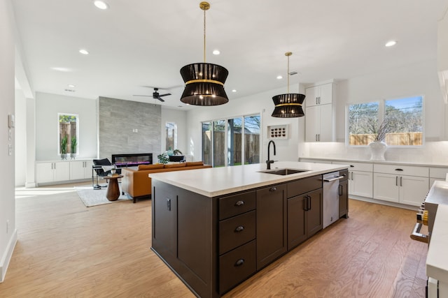 kitchen featuring hanging light fixtures, an island with sink, sink, and white cabinets