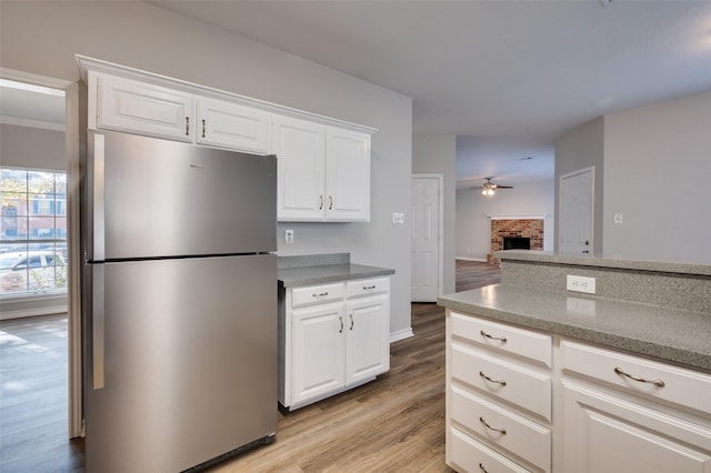 kitchen with a brick fireplace, white cabinetry, stainless steel fridge, and ceiling fan